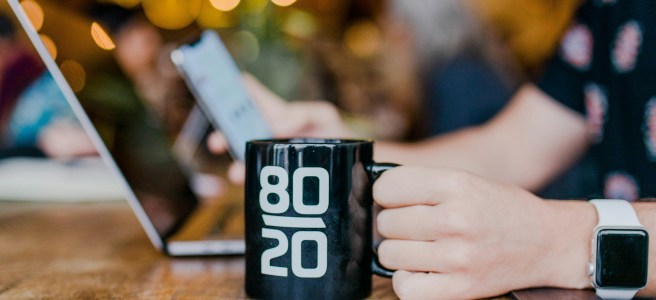 Person holding a coffee mug with '80/20' printed on it, symbolizing the Pareto Principle for productivity and focus.