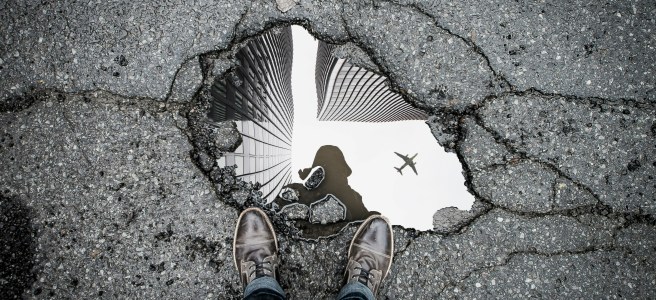 Reflection of a person and buildings in a puddle on cracked asphalt, symbolizing self-reflection and personal growth.