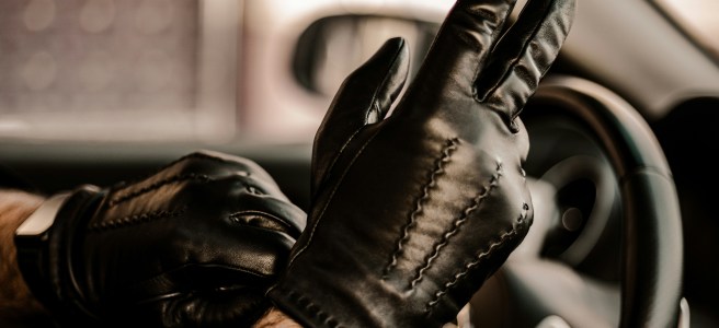 Hands adjusting black leather gloves while gripping the steering wheel, symbolizing readiness, focus, and a touch of rebellion.