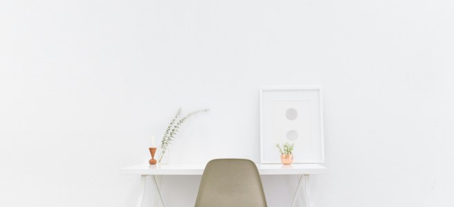 A clean, minimalist desk setup with a chair, small plants, and a framed artwork, symbolizing focus and personal development.