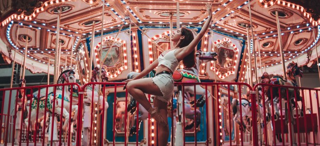 Ballet dancer in casual clothing performing in front of a brightly lit carousel, capturing creative expression and joy.