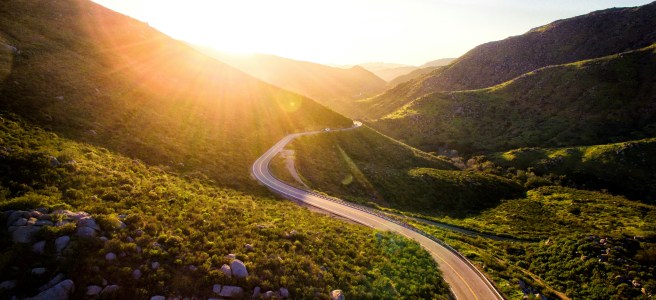 A winding road through green mountains under a bright sunrise, representing the journey of balancing control and navigating life's uncertainties.
