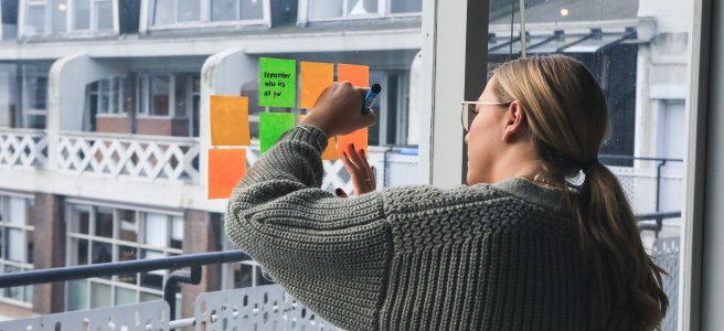 A person writing on sticky notes on a window, symbolizing brainstorming, reflection, and collaboration.