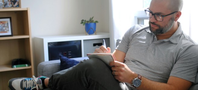 A man sits on a sofa, writing in a notebook, reflecting in a calm and cozy environment—emphasizing the importance of making space for creativity.